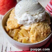 Easy Gluten Free Apple Cobbler with Fluffy Biscuit Topping 10 a serving of gluten-free apple cobbler in a white bowl with apples in the back ground