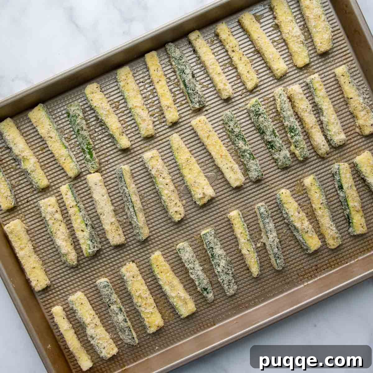 Unbaked zucchini sticks carefully arranged on a well-greased baking sheet.