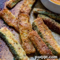 close up of baked zucchini fries on a baking sheet with dip in background