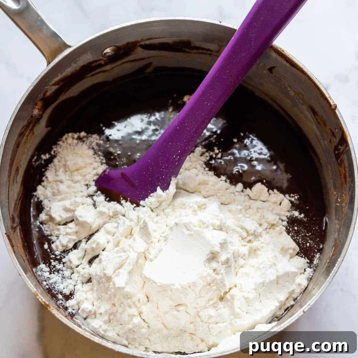 Flour being gently folded into the luscious brownie batter, preparing it for baking. The mixture promises a rich and fudgy base for the decadent brownie layers.
