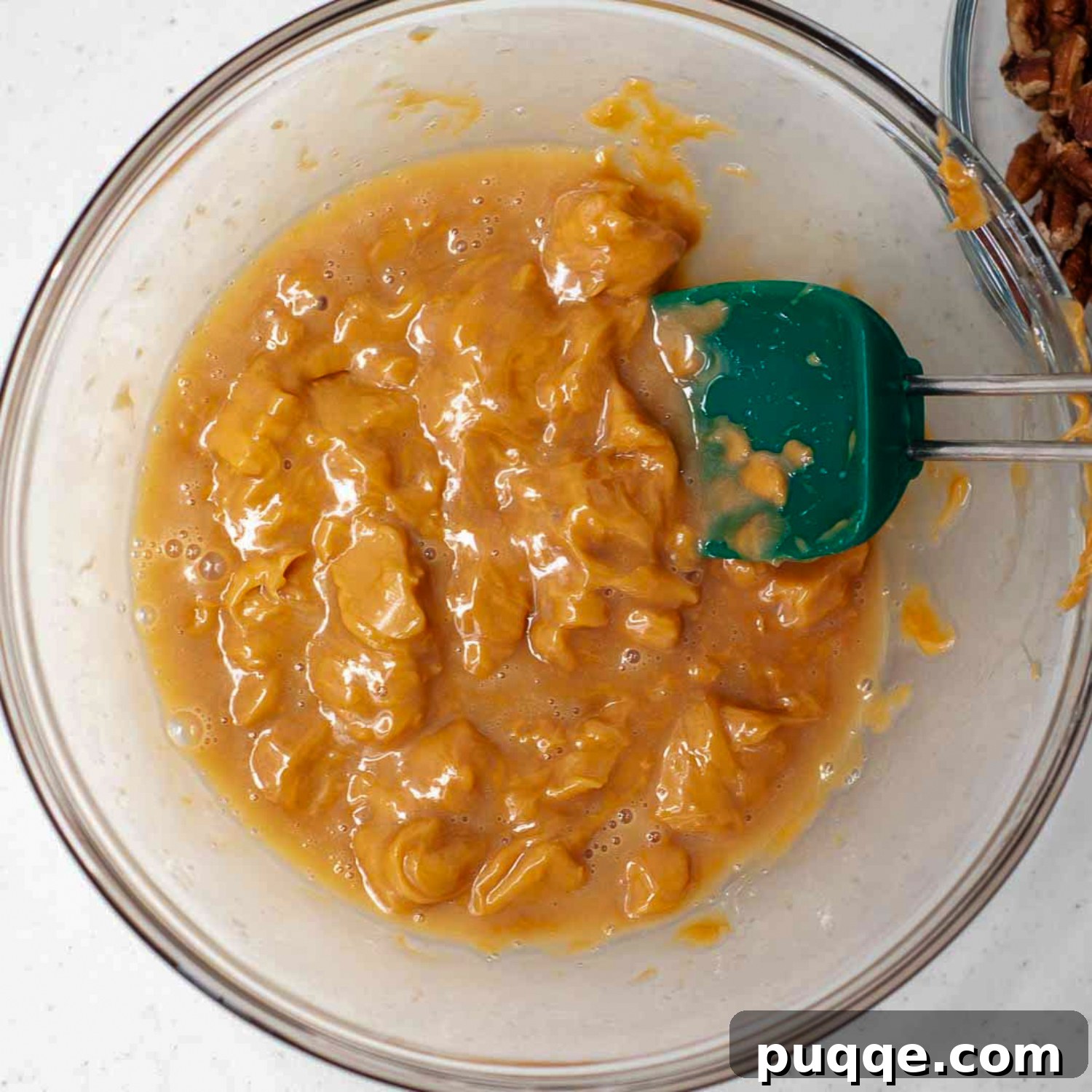 A close-up of caramels and milk melting together in a bowl, showing the perfect 'almost melted' consistency before being fully stirred. This ensures a perfectly gooey texture for the turtle topping.