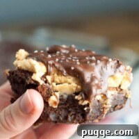 Close-up of a stack of Buckeye Turtle Brownies, showcasing the layers of fudge, peanut butter, and caramel pecans, topped with a chocolate drizzle.