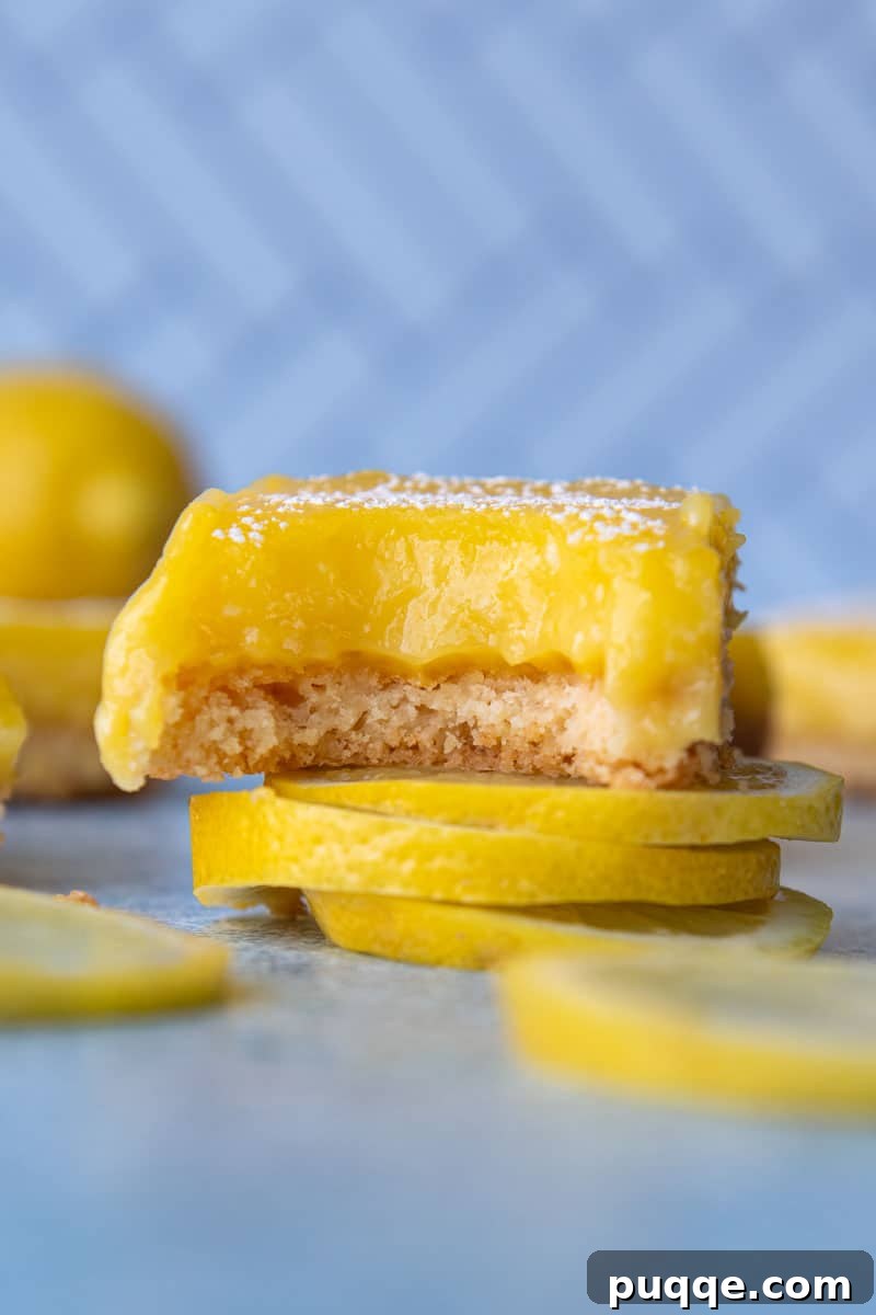 A gluten-free lemon bar with a bite taken out, resting on top of sliced lemons, showcasing its tender texture and bright yellow filling.