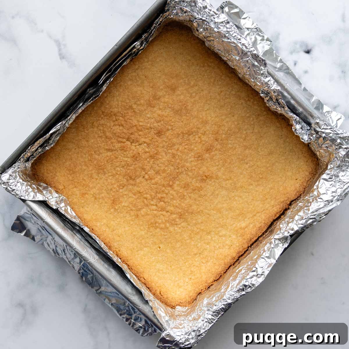 A partially baked shortbread crust in an 8x8 inch pan, showing lightly golden edges.