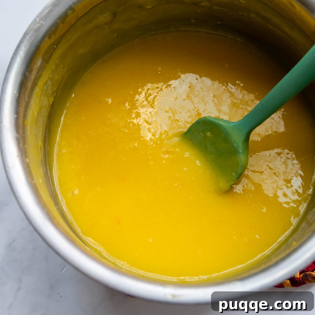 Thickening lemon filling in a saucepan on the stove, being stirred with a spoon, before it's poured over the crust.