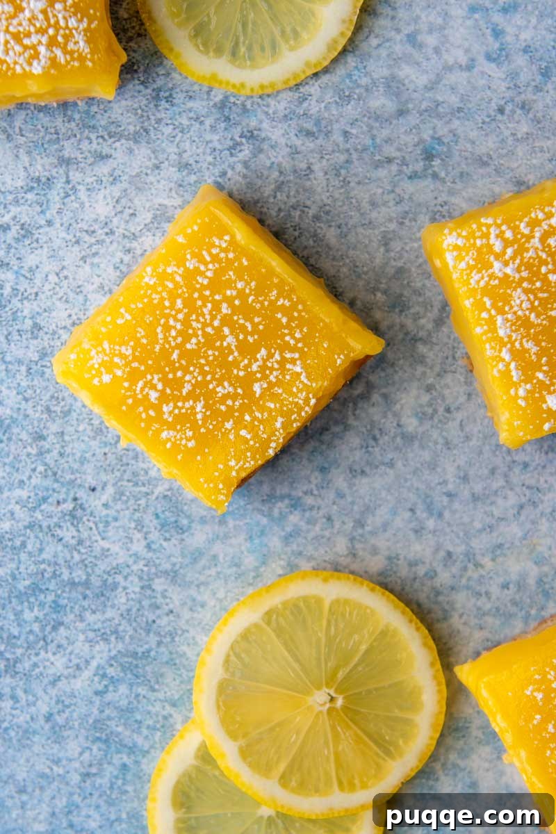 An overhead shot of neatly cut gluten-free lemon bars arranged on a blue background, accompanied by fresh lemon slices.
