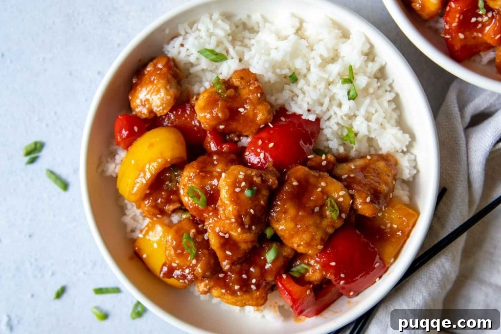 Crispy Baked Gluten-Free Sweet and Sour Chicken 7 Overhead shot of sweet and sour chicken in a white bowl with a side of rice, garnished with green onions.