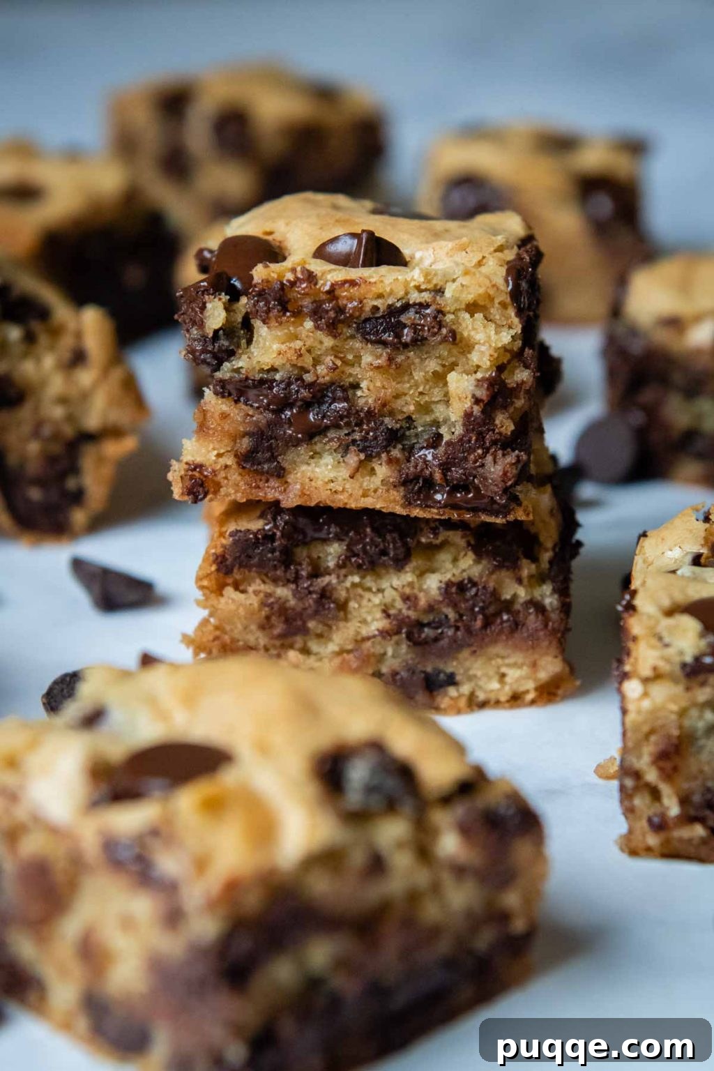 A stack of two perfectly cut gluten-free blondies, with more cut bars and chocolate chips scattered around, highlighting their inviting texture.