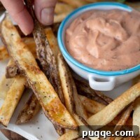 Foolproof Crispy Homemade Oven Fries 7 fingers picking up an oven baked fry on a white plate with a small bowl of fry sauce