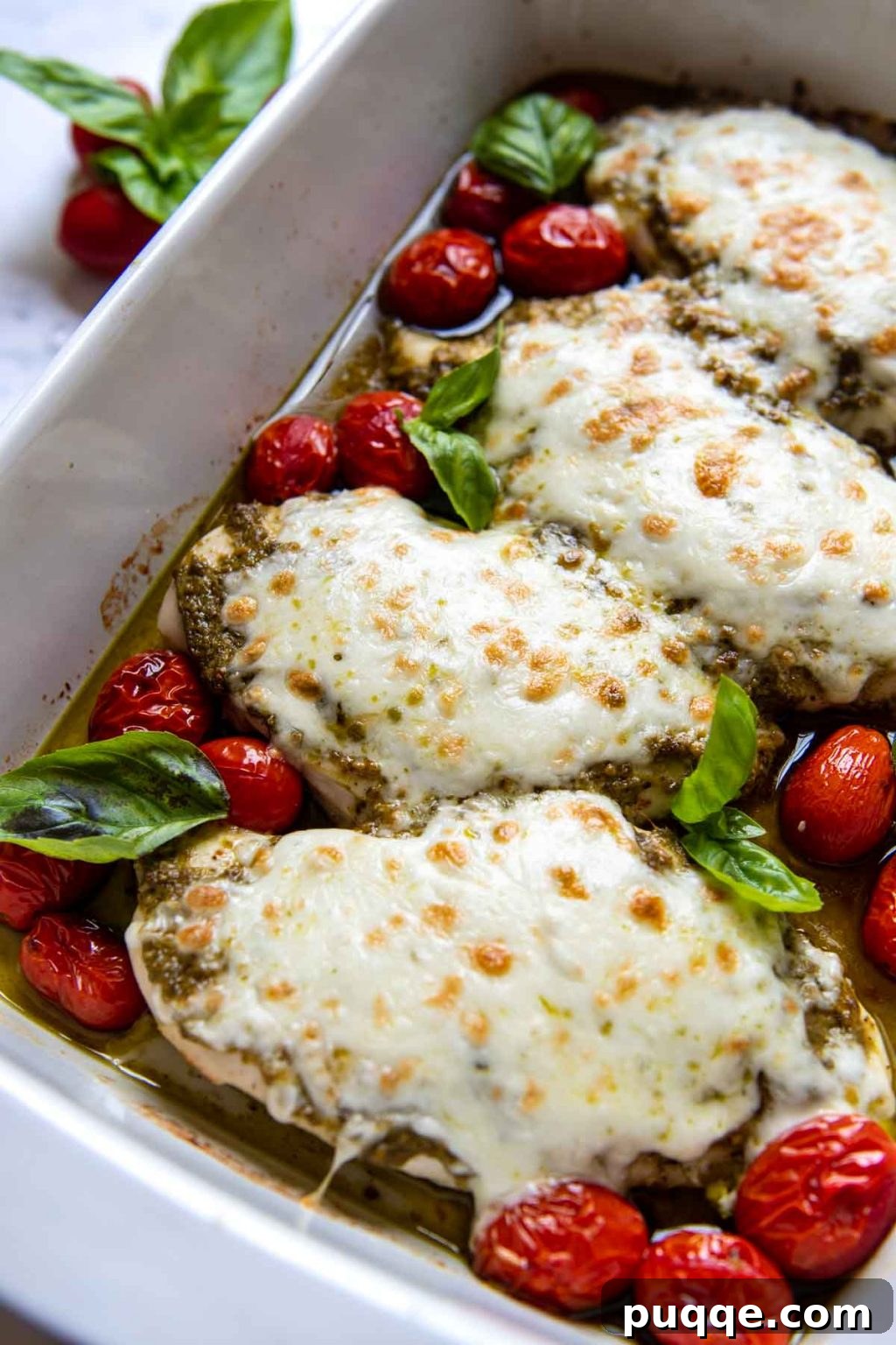 A vibrant close-up of pesto chicken with perfectly melted mozzarella cheese in a white baking dish, showing off the rich textures and colors, ready to be enjoyed.