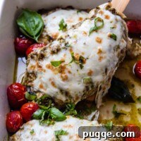 A wooden spatula holding up a chicken breast covered in pesto and mozzarella cheese