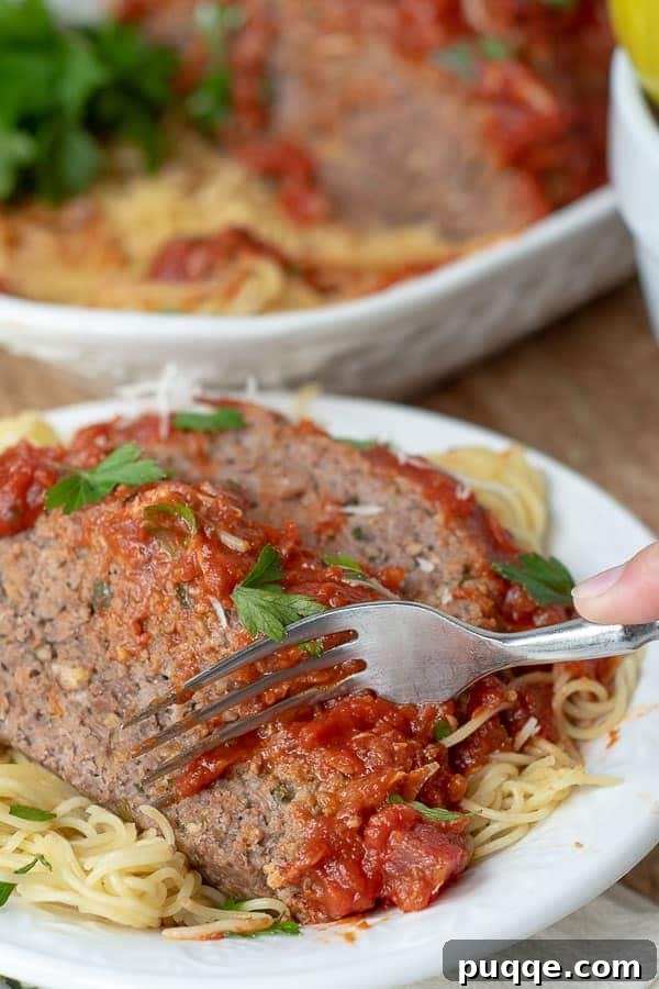 a fork cutting into a slice of Italian meatloaf served on a plate of pasta