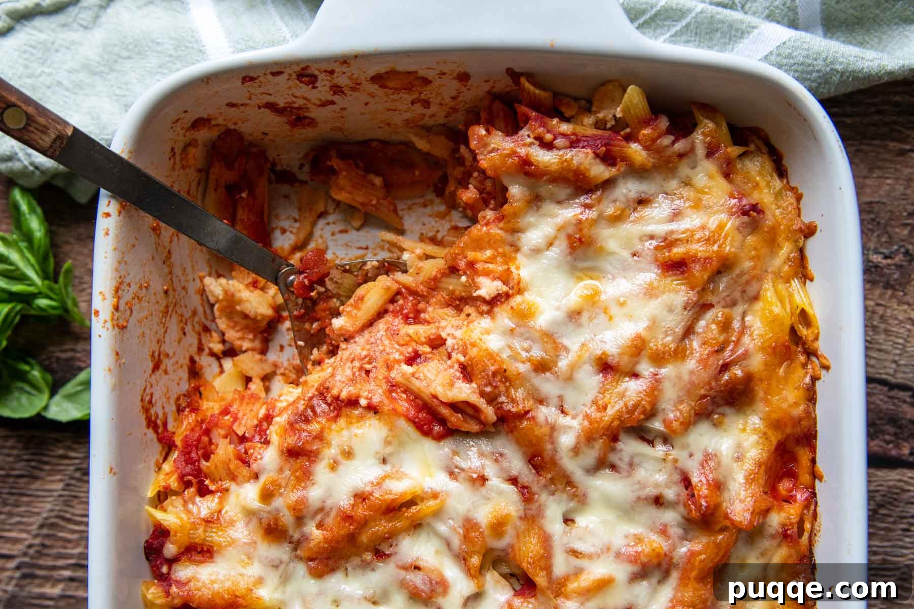 A serving spoon lifting a generous portion of cheesy, saucy baked pasta from a casserole dish, highlighting the texture and layers.