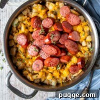 overhead shot of sausage and potatoes in a silver skillet with a blue towel laying next to it