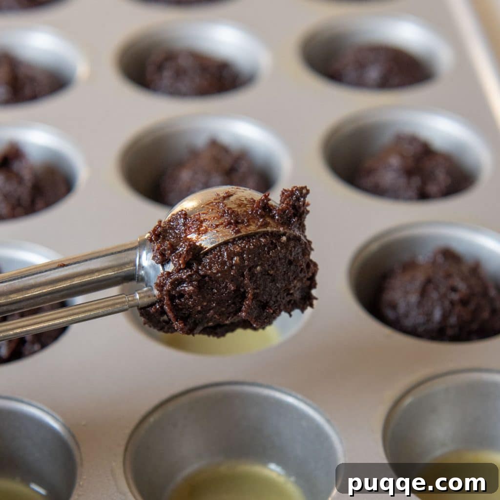 Irresistible Chocolate Financiers 4 a cookie scoop putting uncooked dough in a mini muffin pan