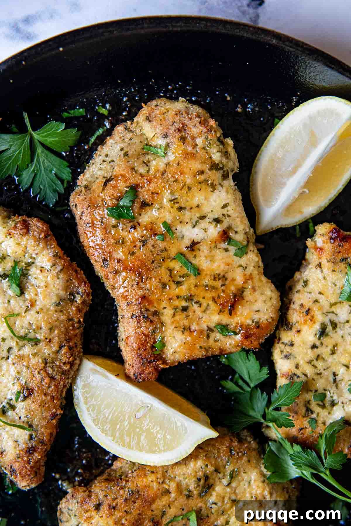 Crispy Almond Crusted Baked Pork Chops Gluten Free 5 Overhead shot of perfectly cooked, breaded pork chops arranged in a black pan, garnished with fresh lemon wedges and herbs.