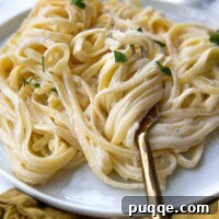A fork twirling a mound of gluten-free fettuccine alfredo on a plate, ready to be eaten.