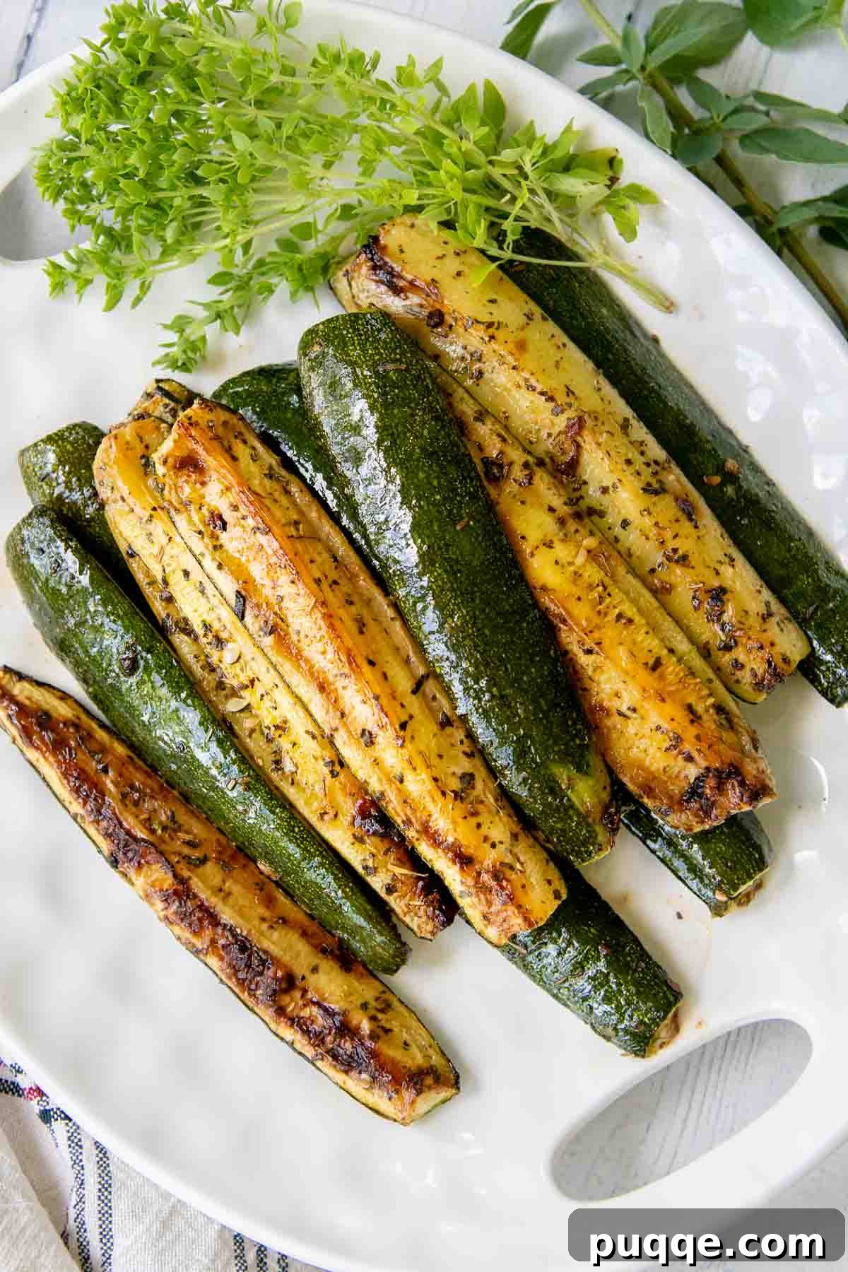 roasted zucchini on a white plate with fresh herbs next to it.