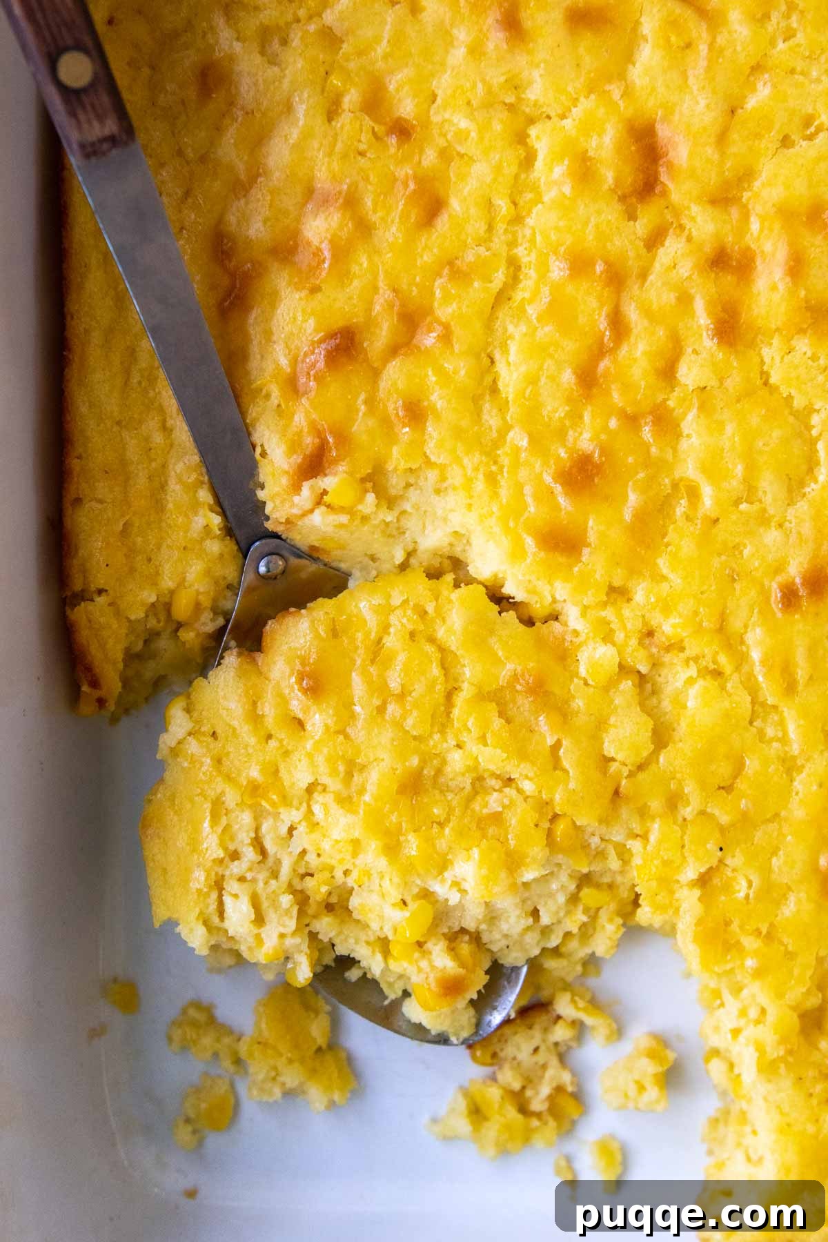 Creamy Fluffy Gluten Free Corn Casserole Made Simple 5 A large serving spoon scooping out a portion of creamy gluten-free corn casserole from a baking dish.