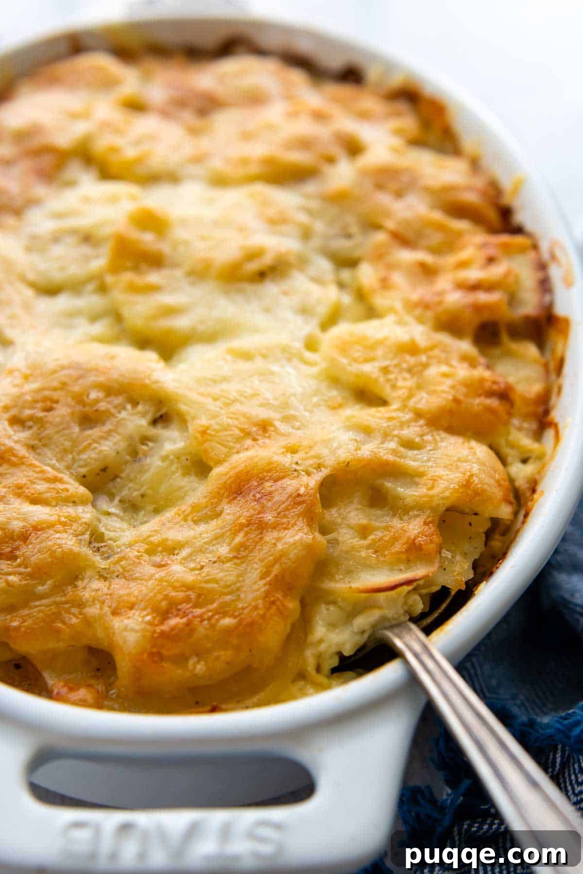 A serving spoon gracefully delving into a pan of golden-brown baked au gratin potatoes, revealing the creamy layers beneath the cheesy crust.