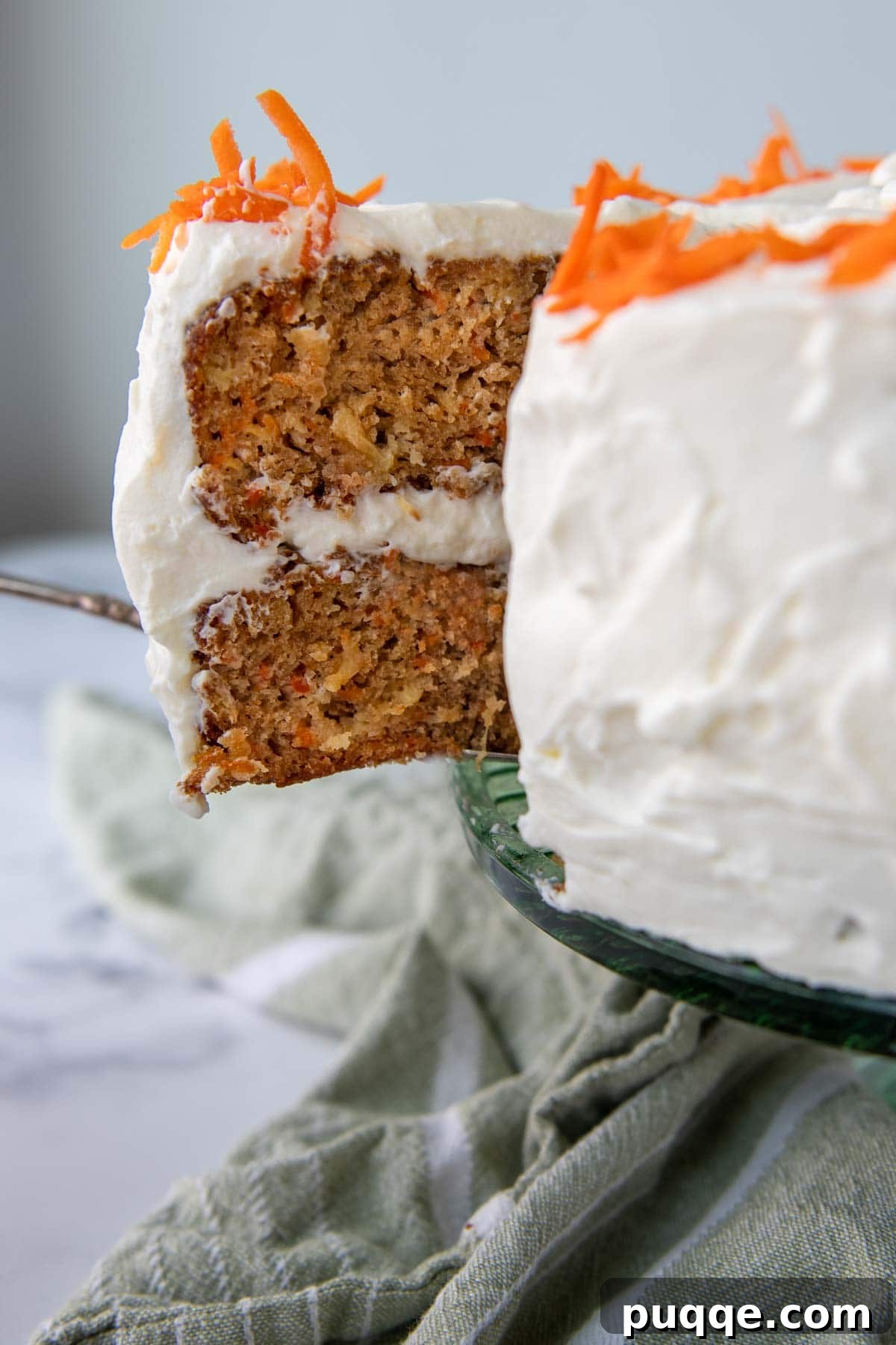 A close-up image of a slice of moist Old Fashioned Carrot Cake with Pineapple being carefully lifted from a cake stand, revealing its rich layers and inviting texture.