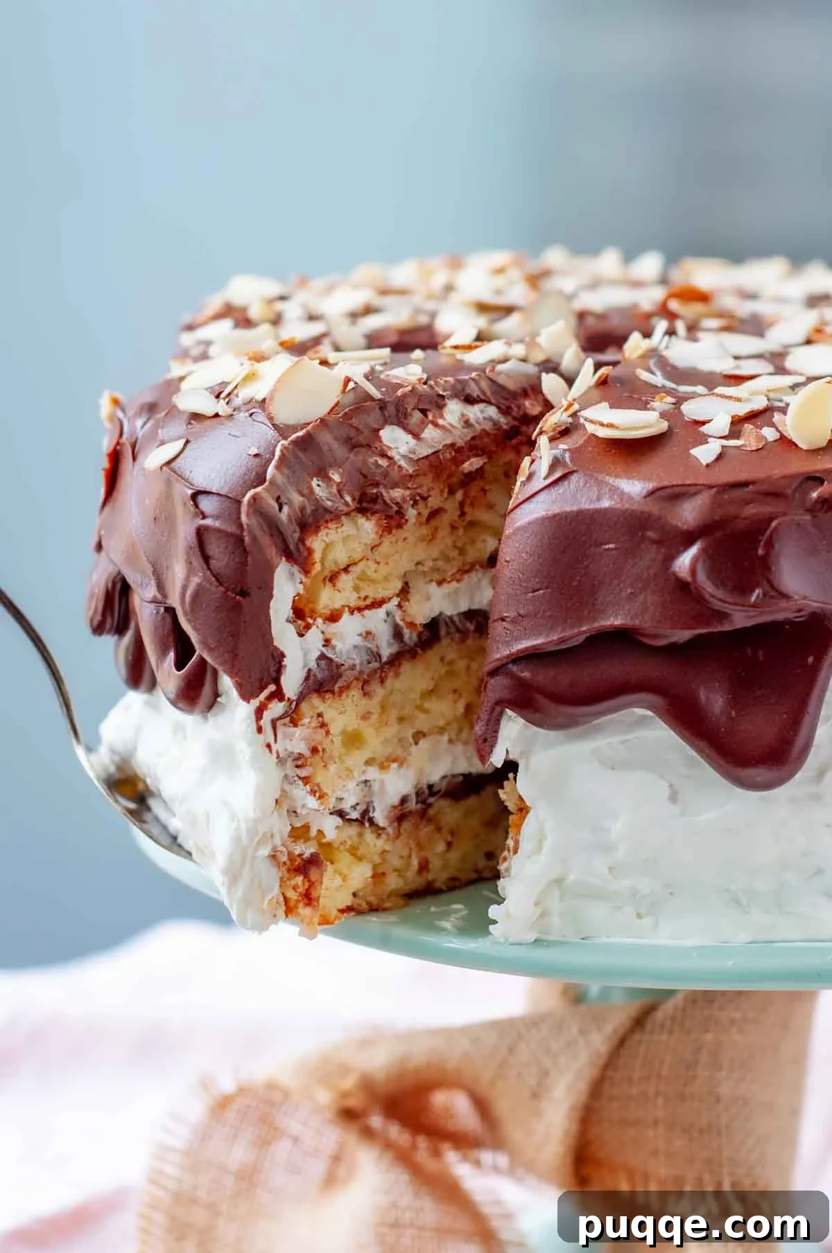 A delicious piece of moist Almond Joy Cake being carefully removed from the whole cake, showcasing its rich layers and fluffy coconut cream frosting.