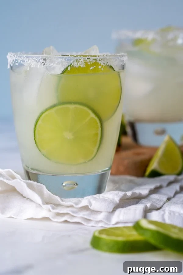 Straight-on shot of a limeade margarita with lime slices next to it