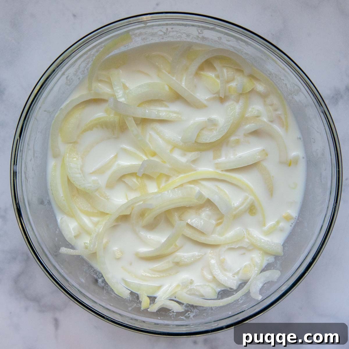 Thinly sliced raw onions soaking in a bowl of buttermilk or soured milk, preparing for frying.