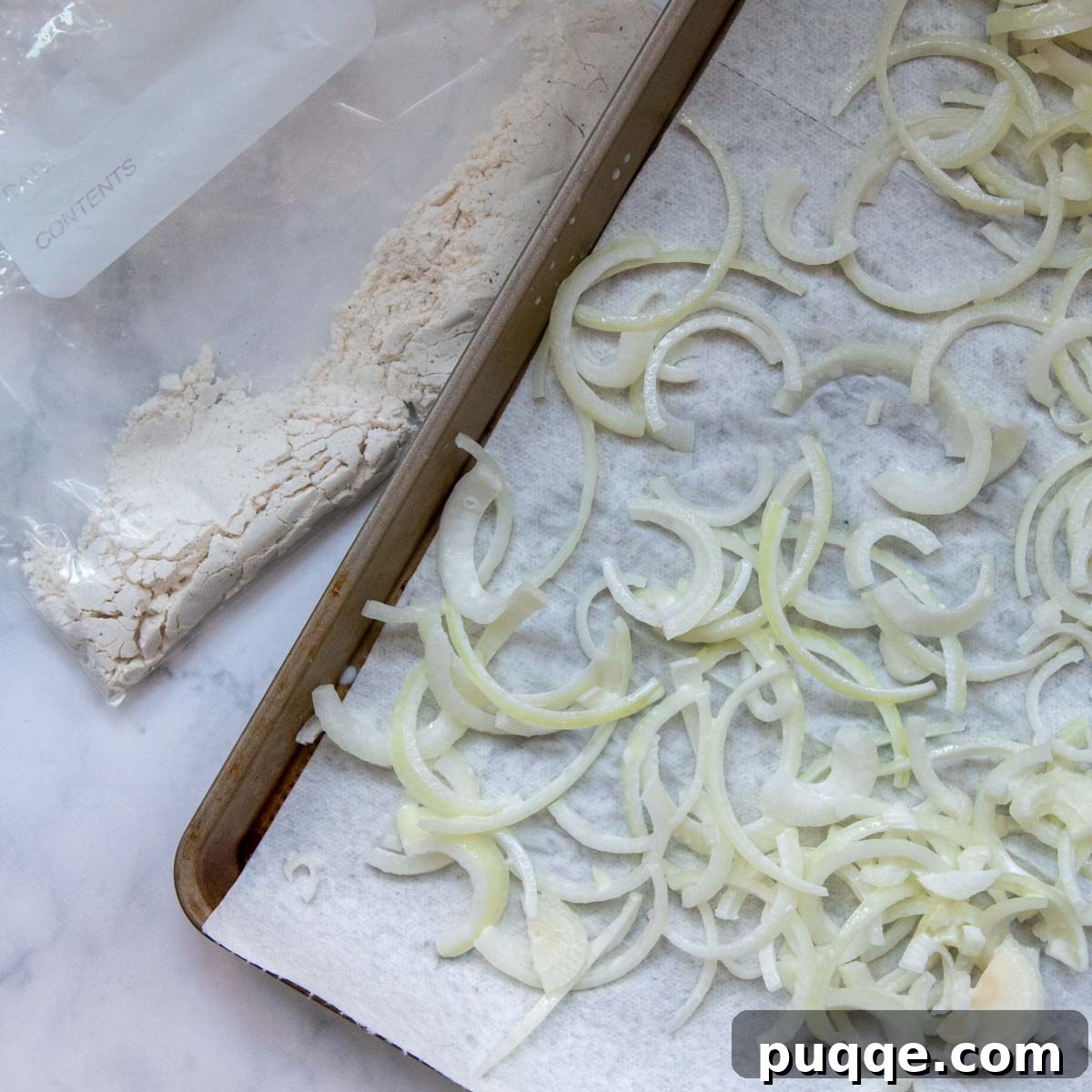 Drained onion slices laid out on a paper-towel lined baking sheet to absorb excess moisture before coating.