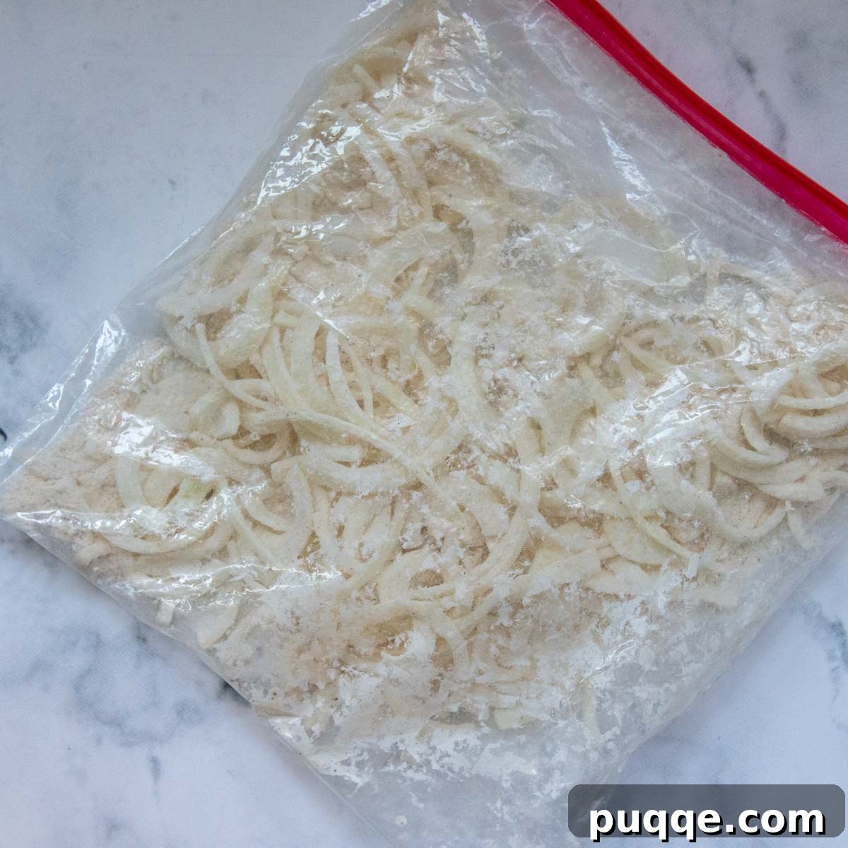 A resealable bag filled with thinly sliced onions thoroughly coated in gluten-free flour, ready for frying.