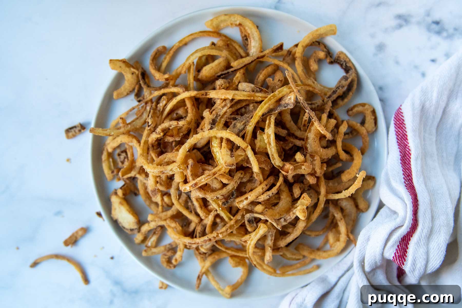 Overhead shot of a white plate filled with golden crispy gluten-free french fried onions, highlighting their perfect texture.