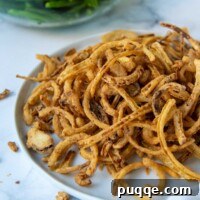 A plate of fried onions with a bowl of green beans behind it, showcasing the delicious homemade gluten-free fried onions.
