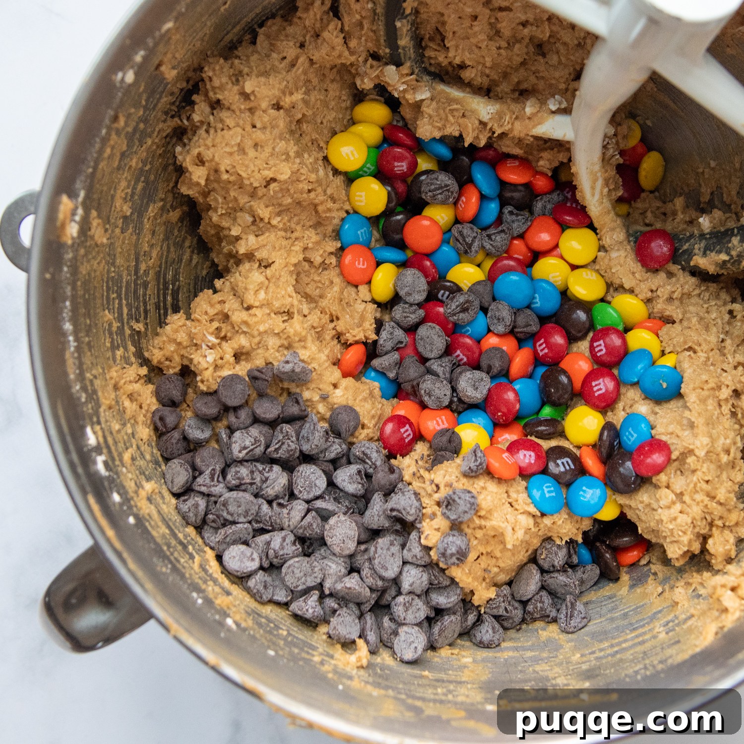 Pillowy Soft Flourless Gluten-Free Monster Cookies 4 A close-up view of the cookie dough in a mixing bowl, generously studded with chocolate chips and vibrant M&Ms, ready for the next step.