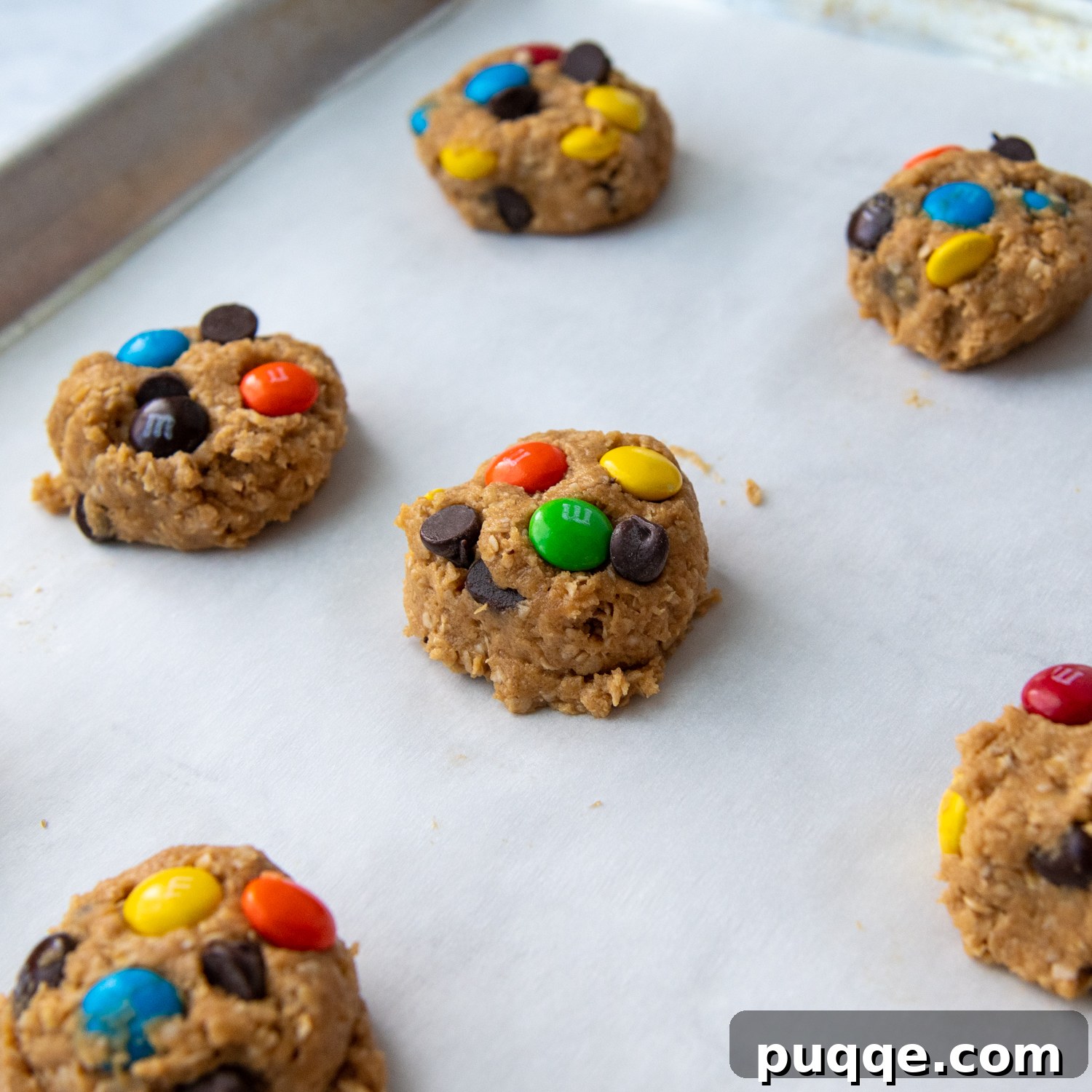 Pillowy Soft Flourless Gluten-Free Monster Cookies 5 Neatly shaped, unbaked monster cookie dough balls, topped with extra M&Ms and chocolate chips, arranged on a baking sheet, ready for the oven.