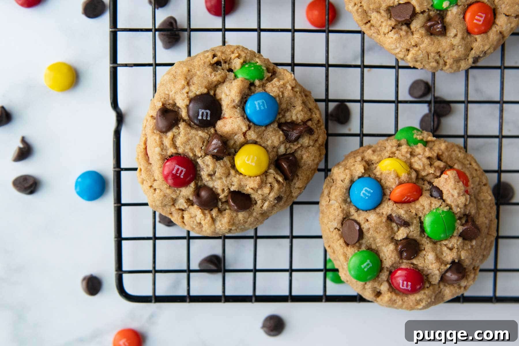 Pillowy Soft Flourless Gluten-Free Monster Cookies 7 Several soft and chewy monster cookies on a wire cooling rack, with colorful M&M candies scattered around, inviting a delightful treat.