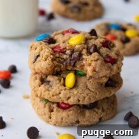 A stack of three monster cookies, with a bite taken out of the top one, showcasing their soft texture and chocolatey goodness.
