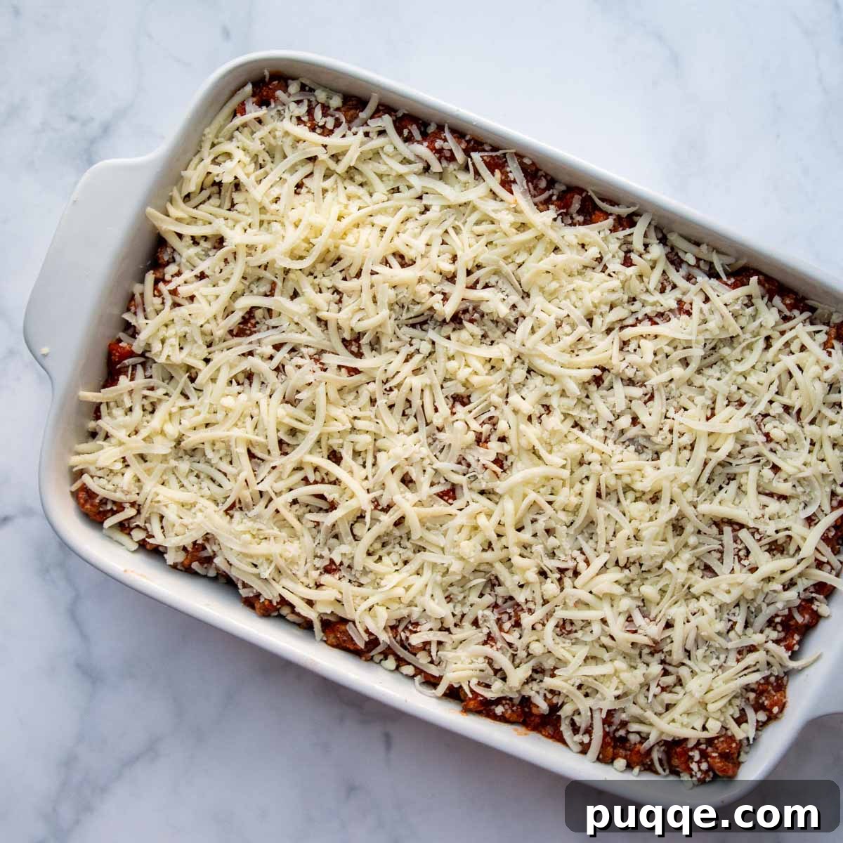 An overhead shot of the beautifully layered, unbaked lasagna in a baking dish, ready for the oven.
