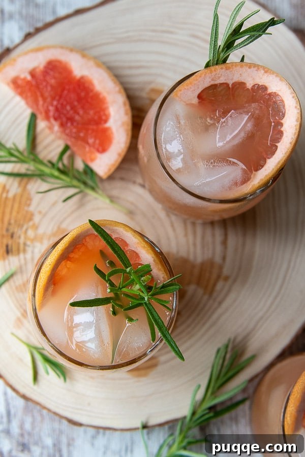 Zesty Grapefruit Vodka Fizz 3 An overhead shot showcasing two expertly crafted sparkling grapefruit vodka cocktails, garnished with fresh rosemary, artfully arranged on a rustic wooden board.