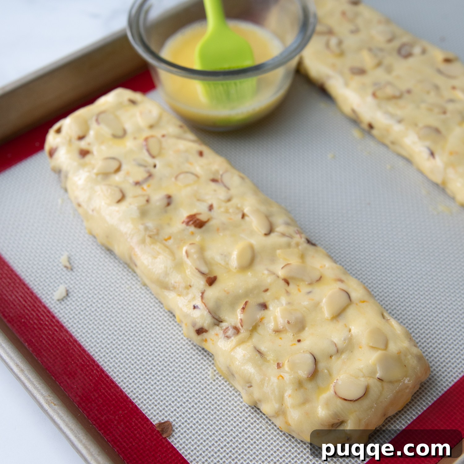 Feather-Light, Perfectly Crispy Gluten-Free Biscotti 5 A pristine biscotti log on a baking sheet, being carefully brushed with an egg wash before its first bake, ensuring a golden, shiny finish.