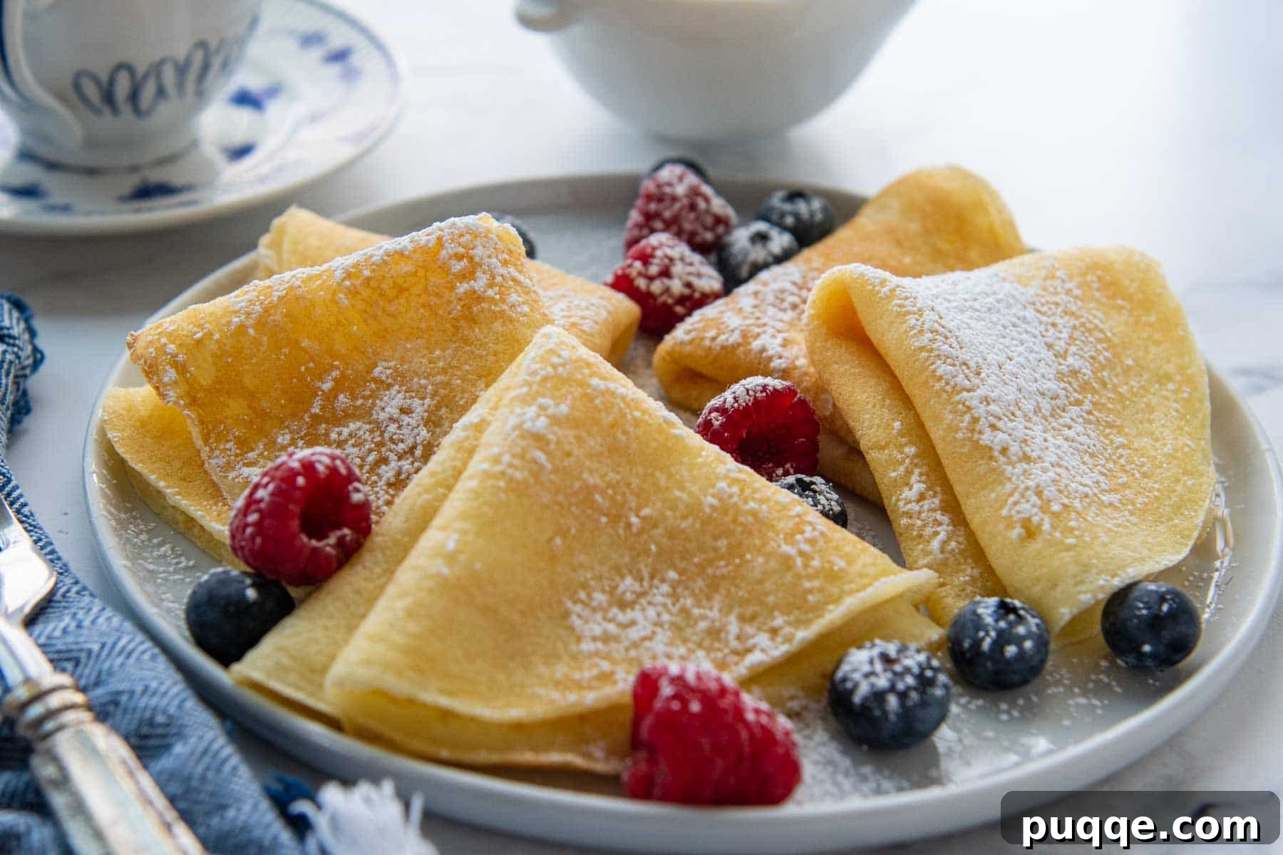 a plate of crepes with powdered sugar and fresh berries
