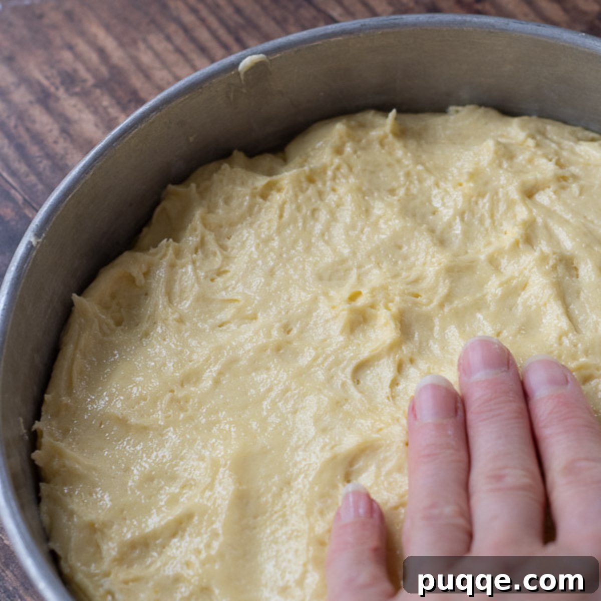 Fingers gently pressing cake batter evenly into a prepared cake pan.