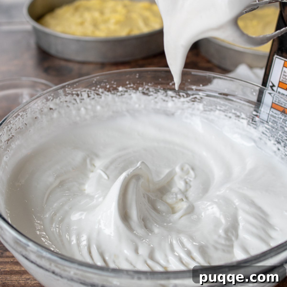 Glossy, stiff peaks of whipped meringue in a clear glass bowl, perfectly prepared.