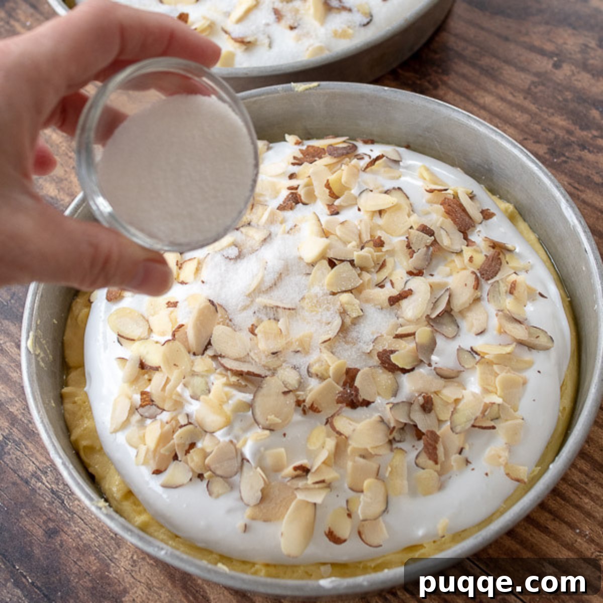 Close-up of granulated sugar sprinkled over sliced almonds on top of a meringue layer.