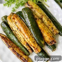 Golden-brown roasted zucchini slices on a white plate, garnished with fresh herbs.