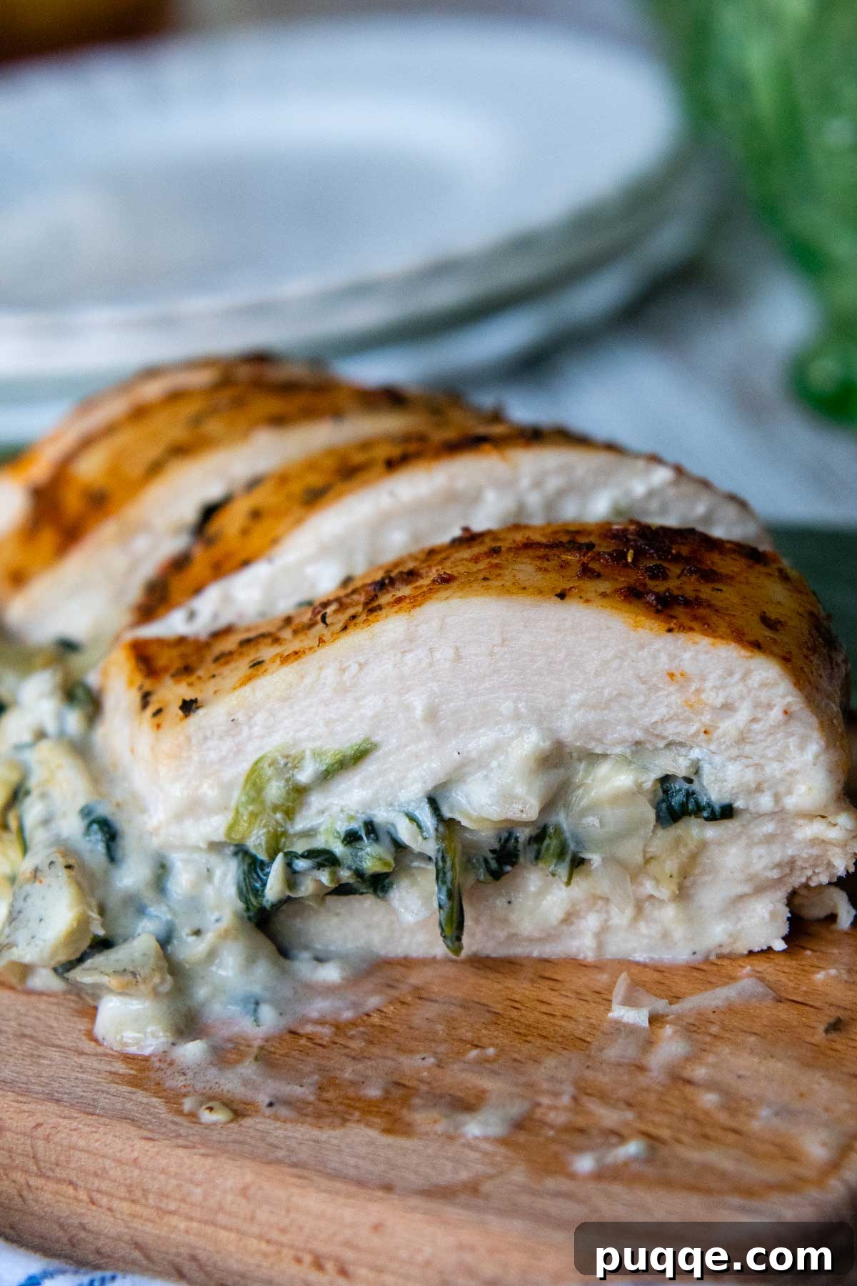 Close up of sliced spinach artichoke chicken on a wooden cutting board, revealing the creamy filling.