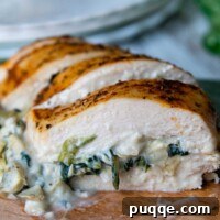 Close up of sliced spinach artichoke chicken on a wooden cutting board, revealing the creamy filling.