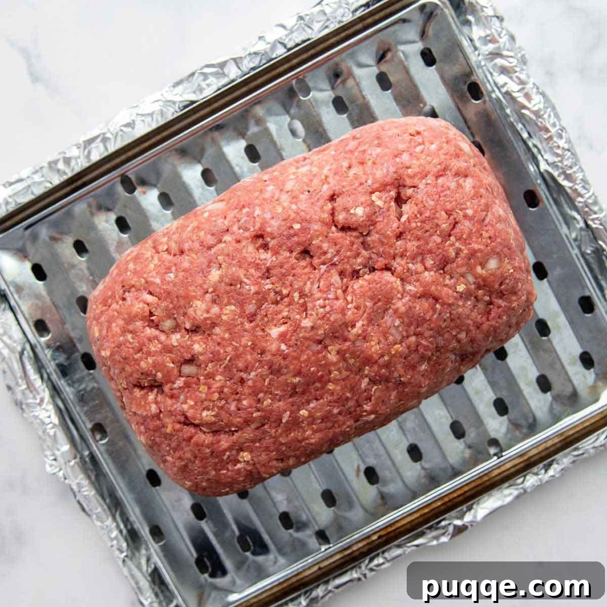 Juicy Gluten-Free Meatloaf: A Taste of Home Comfort 3 A perfectly shaped meatloaf, ready for the oven, resting on a small broiler pan insert within a larger foil-lined baking pan.