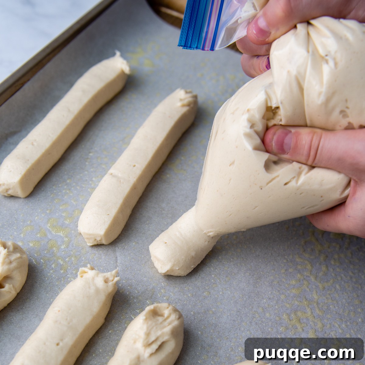 Piping gluten-free breadstick dough onto a baking sheet using a plastic Ziploc bag.