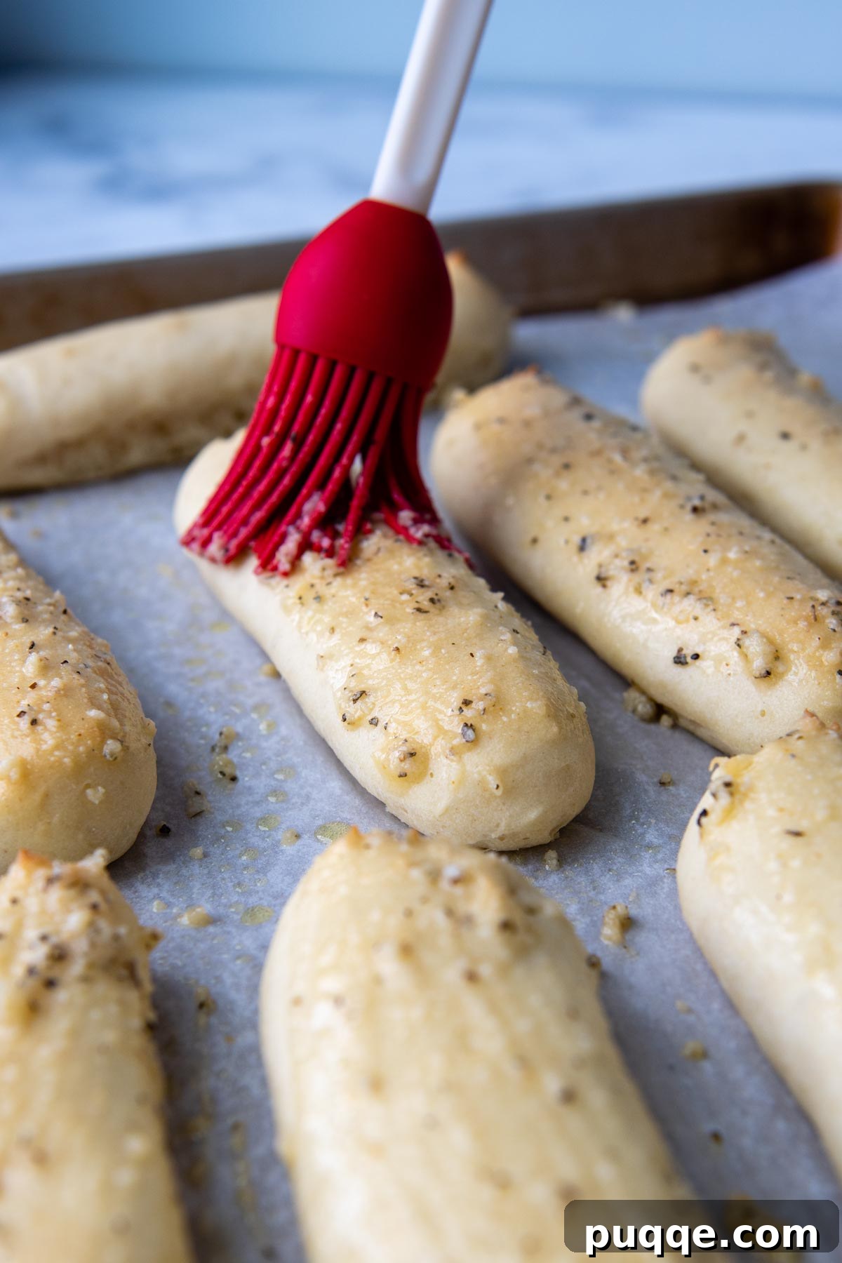 A pastry brush applying melted garlic butter topping onto warm gluten-free breadsticks.