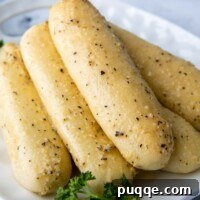 Freshly baked gluten-free breadsticks stacked on a white plate with parsley garnish.